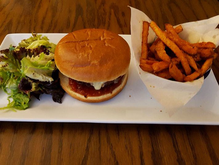 A delicious and well-presented kids meal from The White Bear Pub in Epworth, featuring a cheeseburger with melted cheese and red sauce, served alongside a fresh mixed green salad and a portion of crispy sweet potato fries.