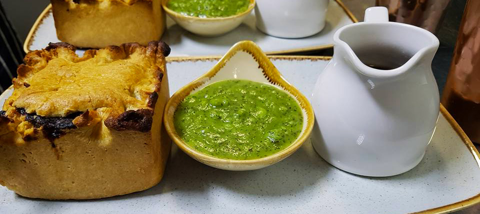 A delicious individual golden-crusted steak and ale pie served with a side of vibrant green mushy peas and a white gravy boat, presented on a light plate at The White Bear Pub & Restaurant in Epworth.