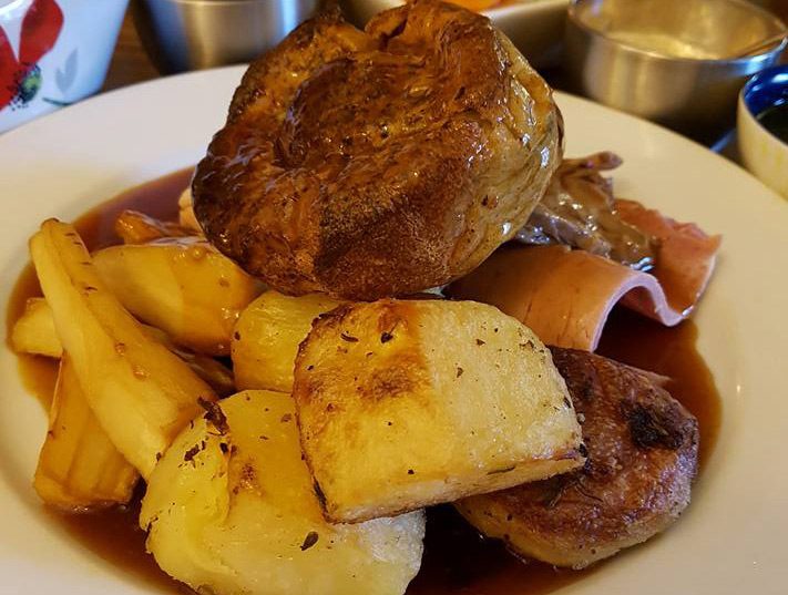 A close-up view of a traditional Sunday lunch plate, featuring a large golden Yorkshire pudding, crispy roasted potatoes, tender parsnips, and succulent roast meat, all generously covered in a rich brown gravy, served in Epworth.